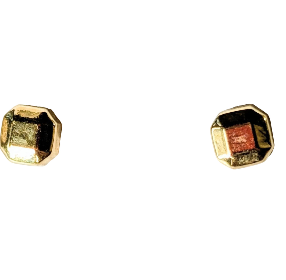 A pair of gold-toned geometric stud earrings with a small square red center stone, displayed on a textured white surface.