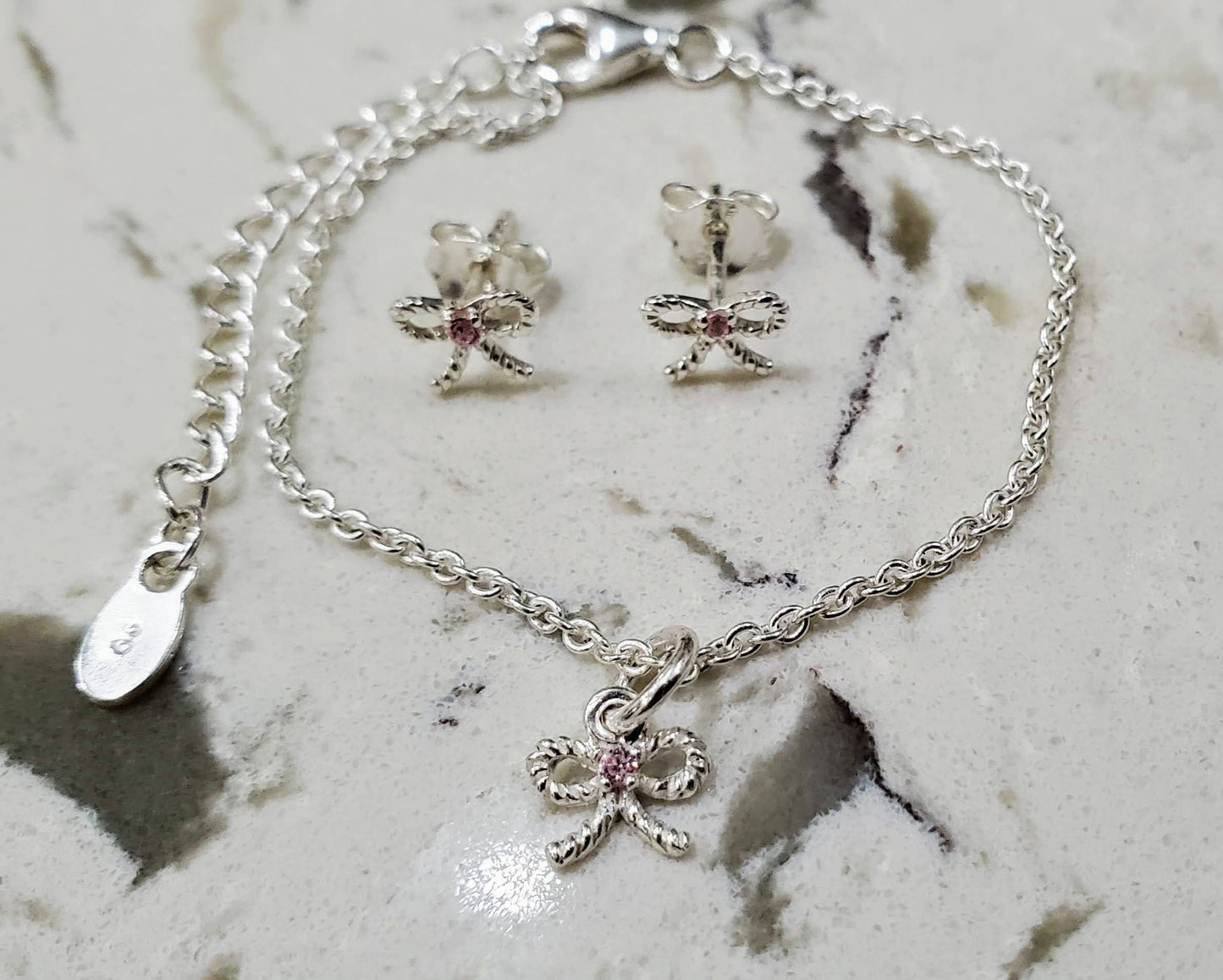 Baby or child's sterling bow bracelet and earrings set with pink CZ stones in the center. Antiqued finish. Bows are twisted shape. Bracelet finished with lobster clasp and 2 inch extender.